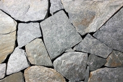 An elegant tinted gray-green stone with some mica flecks. Surface has a smooth, glossy finish. Hand-Split Thin Veneer ranges in thickness from 1" to 3" with a nominal face range of 6" to 18". Average coverage is approximately 100 to 110 square feet per ton. A brick ledge of 4" to 6" is recommended when laying this product as a facade. Packaged in 1-ton Pallets.